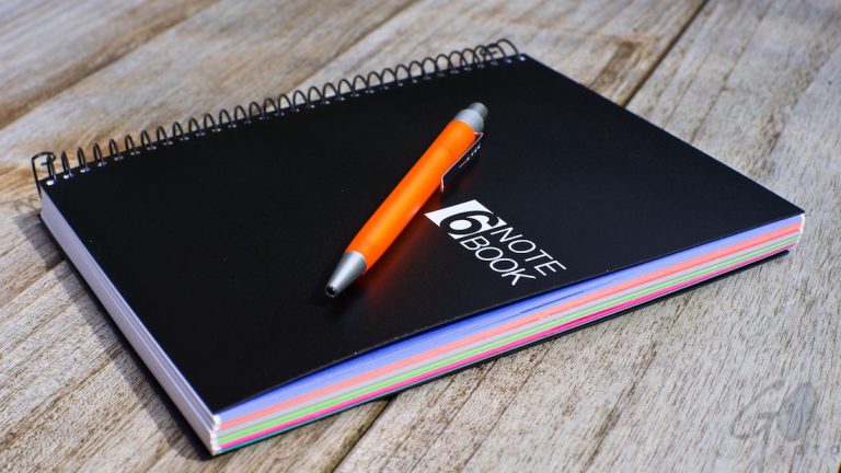 Tekstschrijvers en lezers willen structuur in een verhaal. Foto van een zwart nititieblok met een oranje pen.