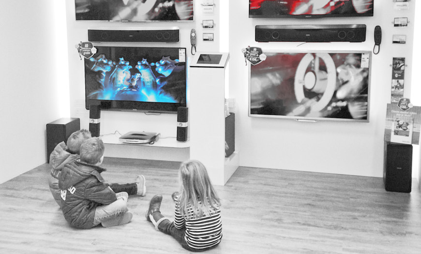 Drie kinderen zittend voor een wand met TV's