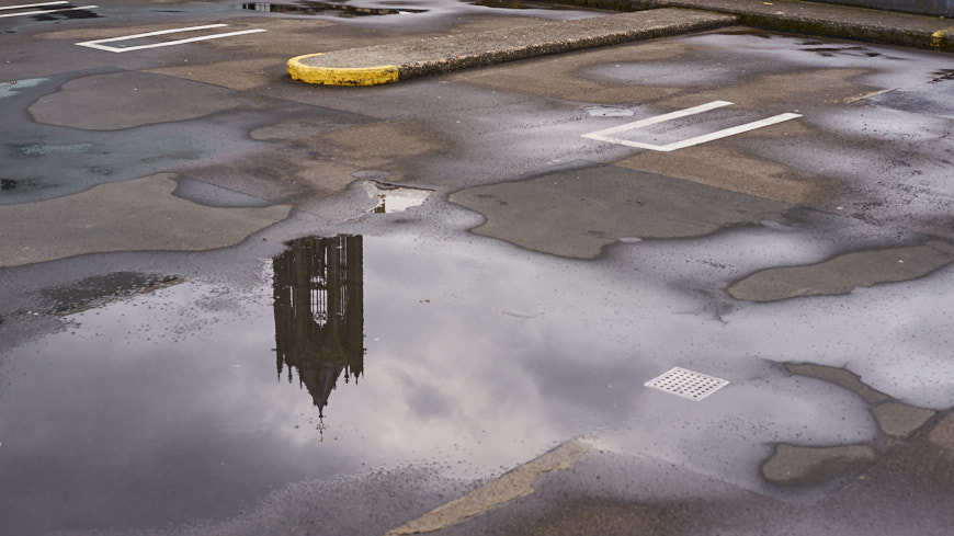 Topje van Domtoren spiegelend in waterplas op parkeerdek