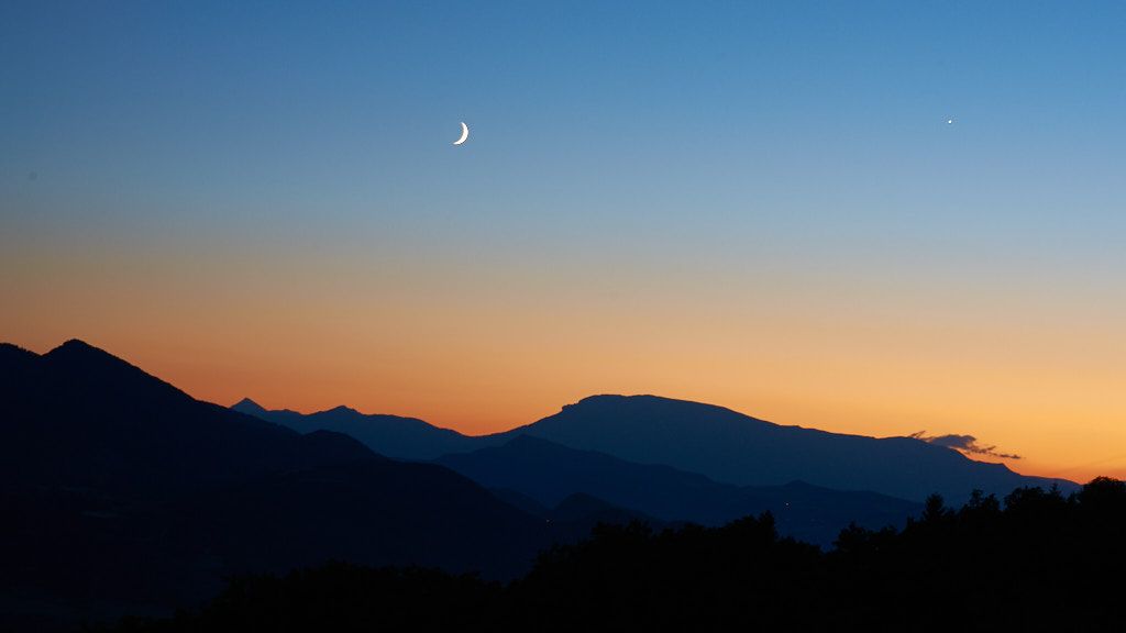 Donkere bergketen met oranje avondlucht en sikkelvormige maan