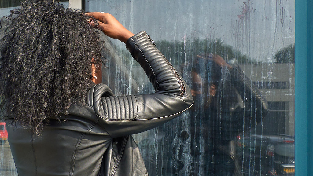 Vrouw inspecteert heur haar in spiegelend raam