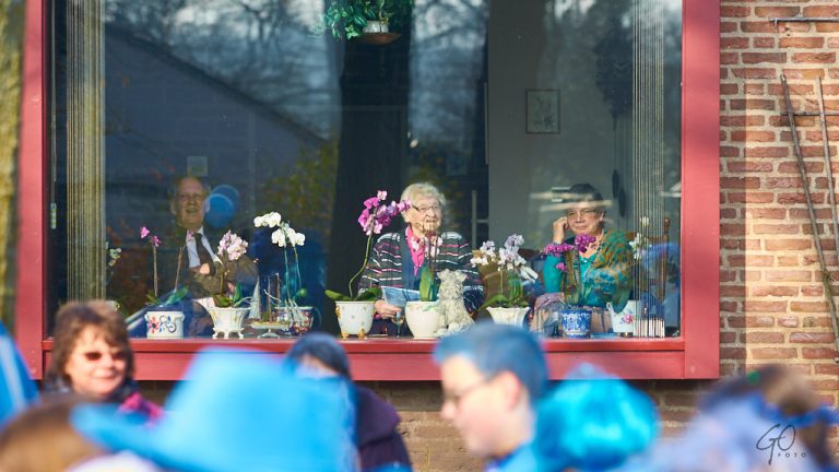 Oude mensen achter raam kijken naar carnavalsoptocht