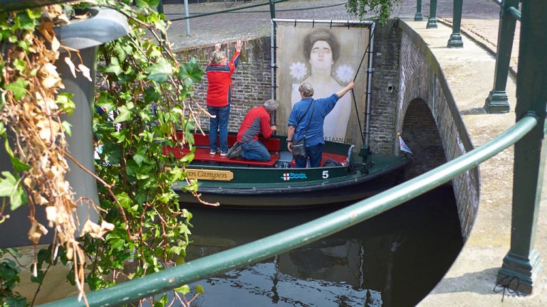 Mensen in boot hangen kunst aan kadewand