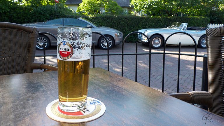 Glas bier op terrastafel, twee cabrio's op de achtergrond